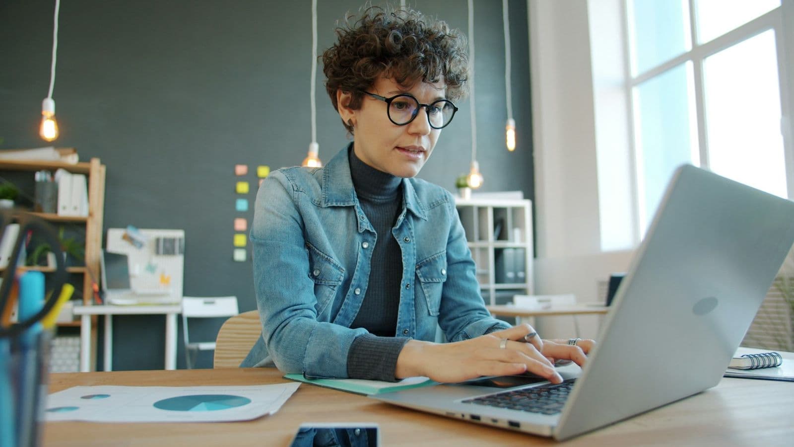 A woman working with focus on a laptop in a bright office
