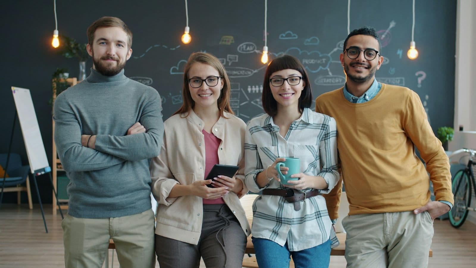 Four colleagues standing side by side in an office, laughing