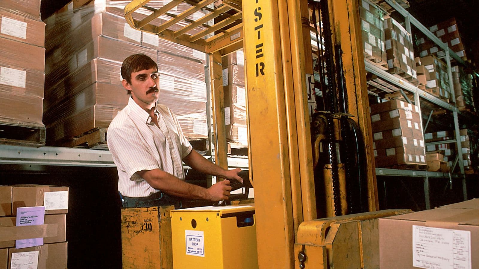 A worker on a forklift in a warehouse full of boxes